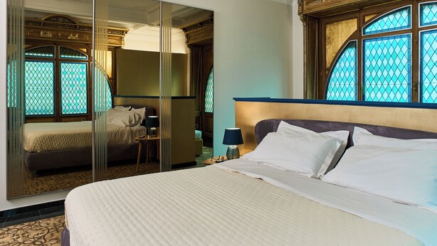 A hotel room with a large bed, a mirror, a nightstand, and a window with a view. - GLAM TIME (Genoa)