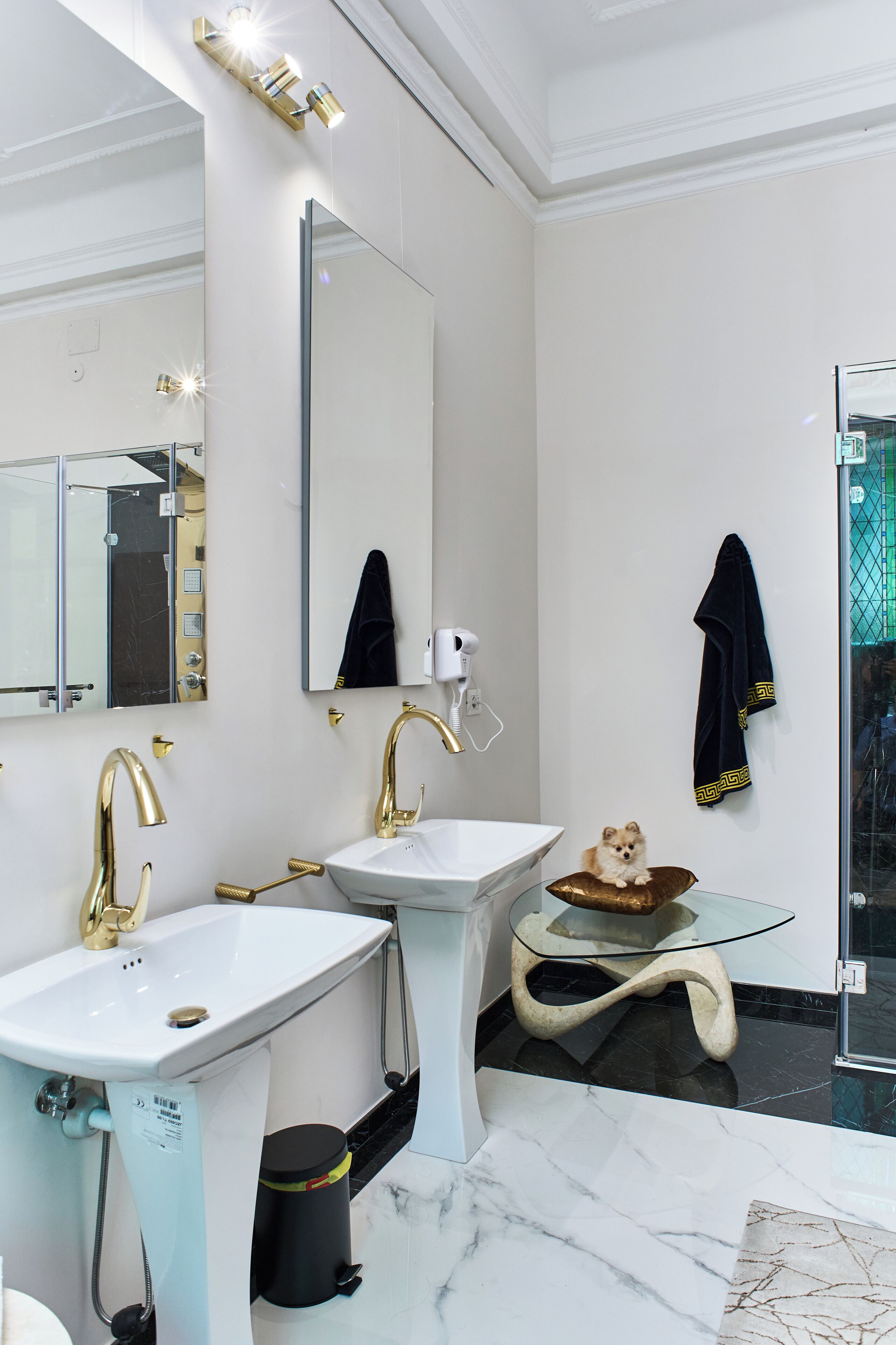 A modern bathroom with two sinks, a large mirror, and a glass table with a towel.