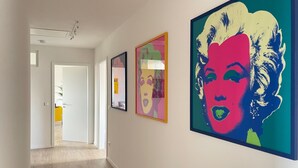 Un couloir avec trois œuvres d’art encadrées accrochées au mur, une porte au fond et un plancher en bois.