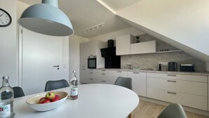 Une cuisine moderne avec des meubles blancs, un four encastré et un coin repas comprenant une table blanche et des chaises noires.