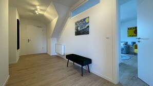 Un couloir avec un plancher en bois, un banc, un radiateur et un tableau accroché au mur.
