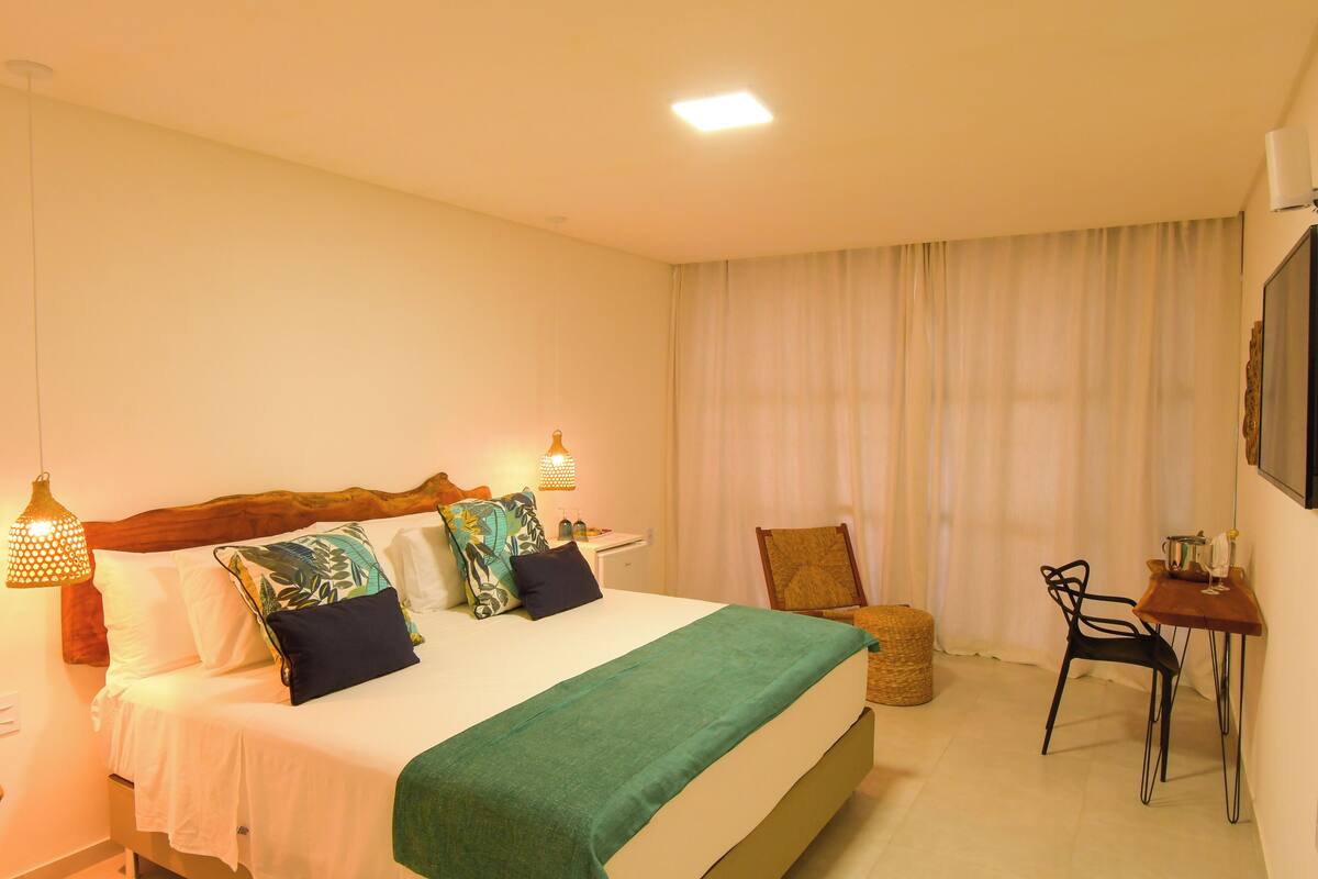 Habitación de hotel ordenada con cama, una mesita, una silla y una lámpara.