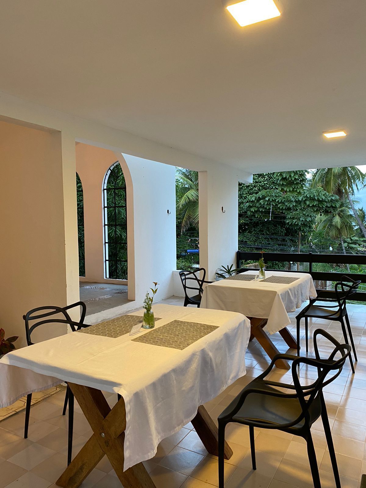 A restaurant with tables set for dining, featuring a view of lush greenery outside.