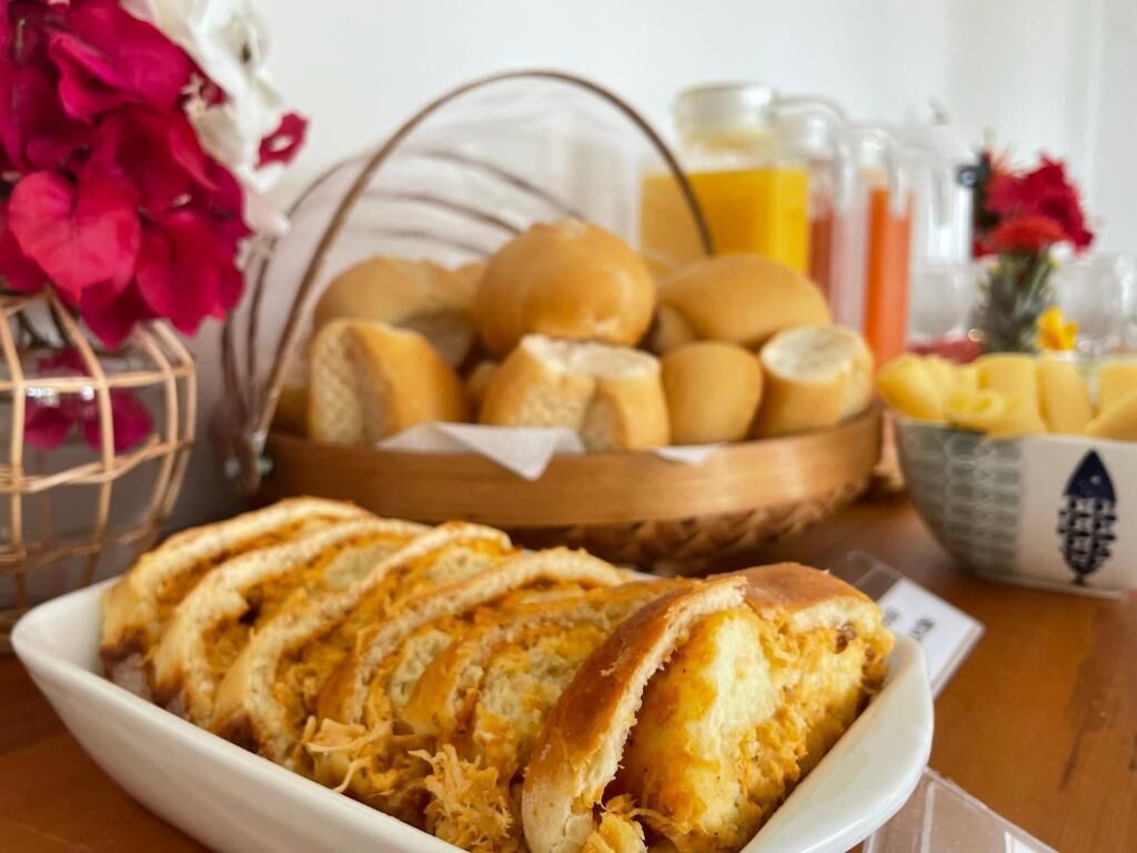 A breakfast setting with bread rolls, sliced bread, and a bowl of fruit.