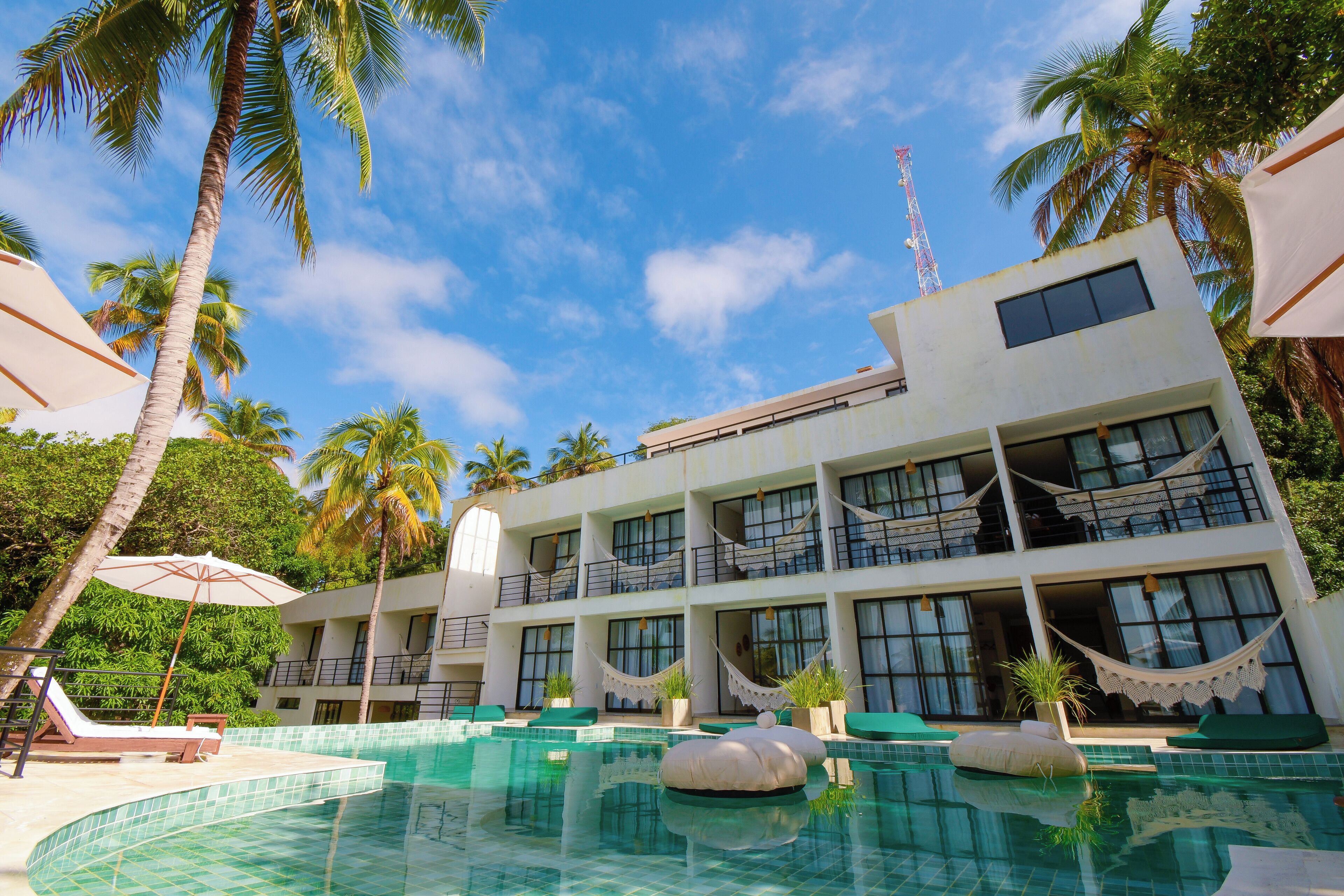 A hotel with a swimming pool, palm trees, and a clear blue sky.