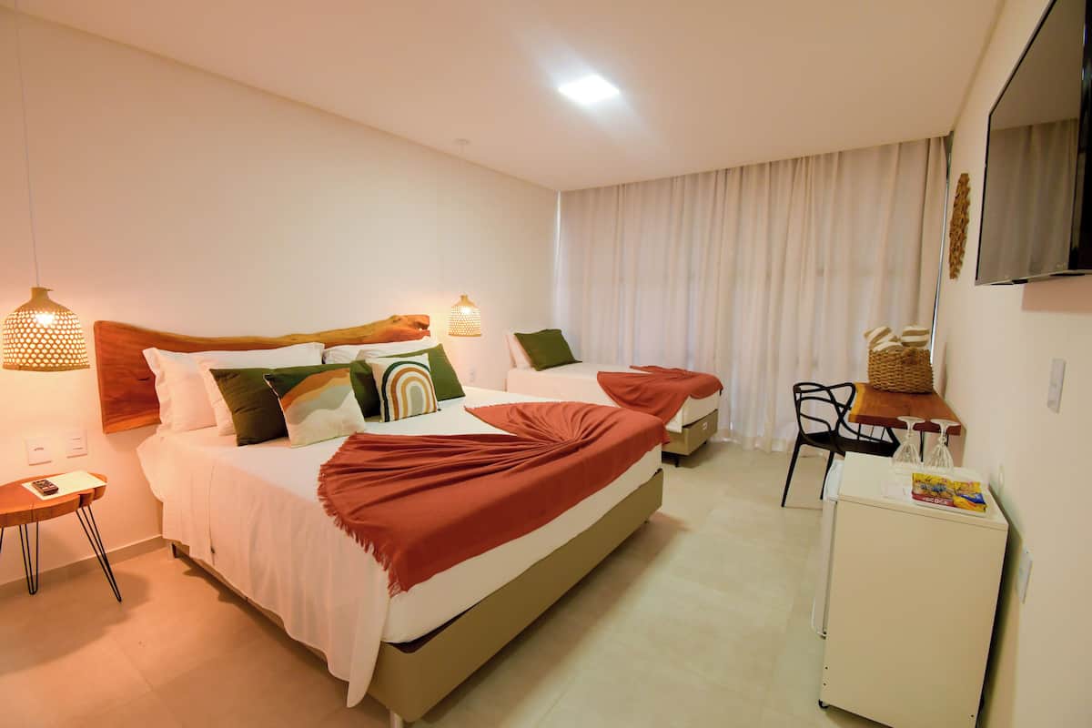 Una habitación de hotel con una cama grande, mesitas de noche, un escritorio, una silla y un refrigerador pequeño.
