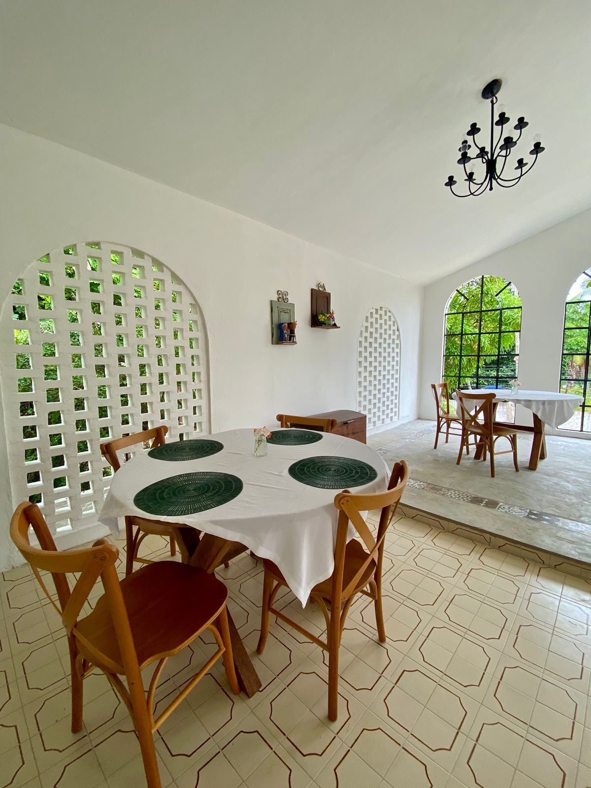 A dining area with a round table, wooden chairs, and a white tablecloth. There are decorative wall sconces and a chandelier.