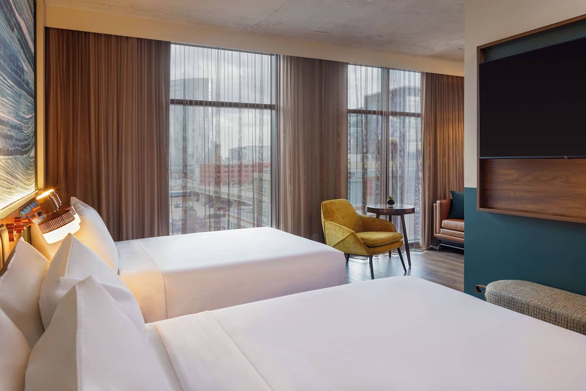 Une chambre d’hôtel avec deux lits, un bureau, une chaise et une grande fenêtre avec des rideaux.