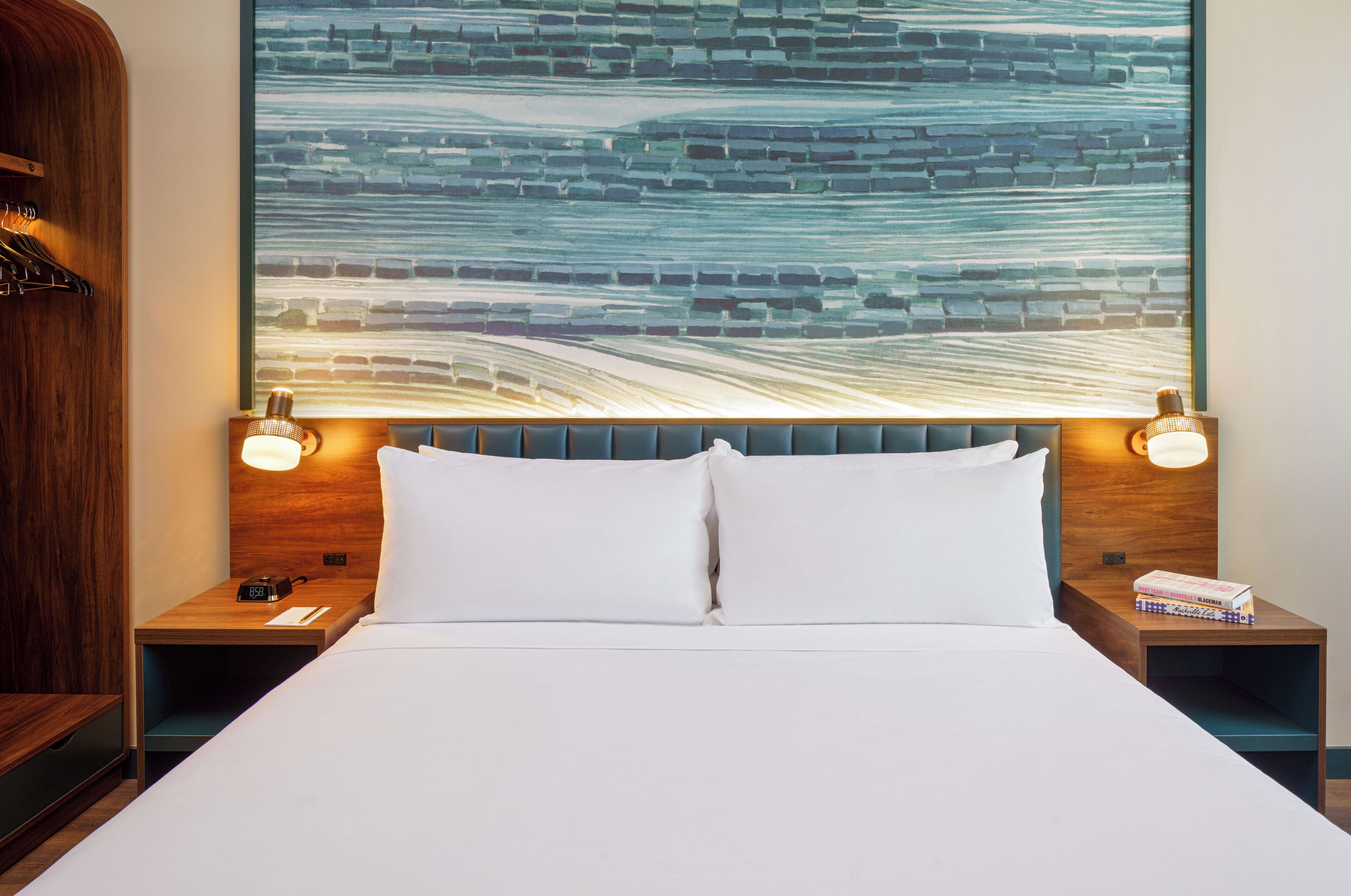 Une chambre d’hôtel avec un grand lit, deux tables de chevet, une tête de lit en bois et une œuvre d’art murale.