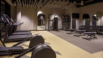 Un gimnasio con cintas de correr, bancos de pesas y mancuernas.
