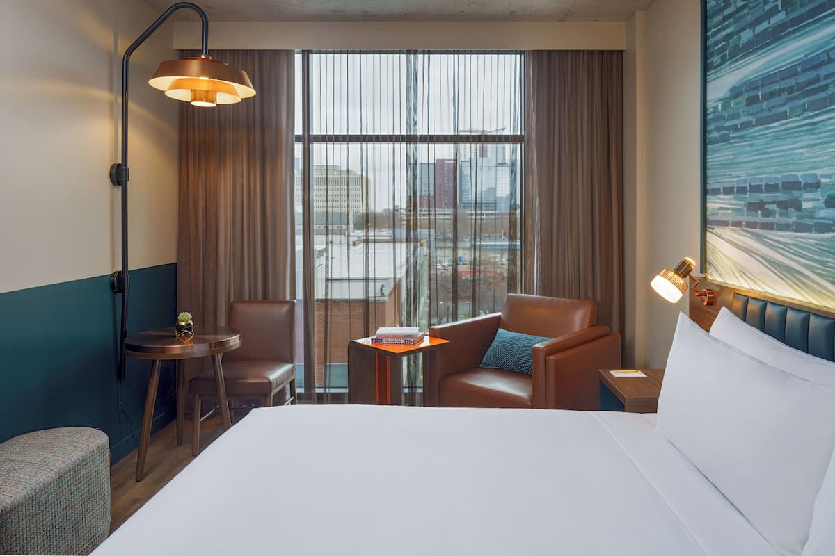 Une chambre d’hôtel avec un lit, deux fauteuils, une petite table et une table de chevet.
