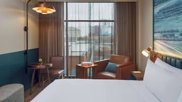 A hotel room with a bed, two armchairs, a small table, and a nightstand.