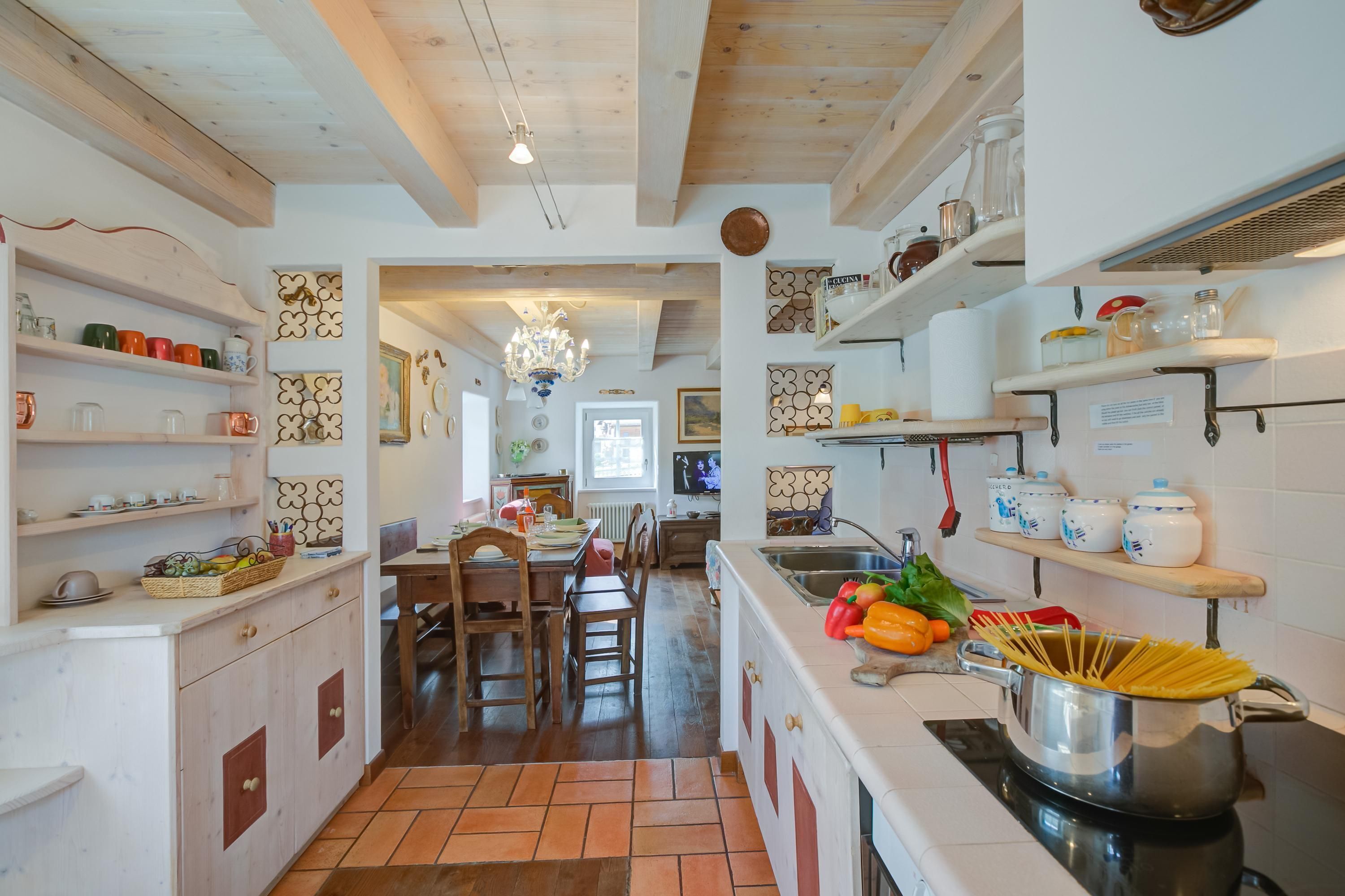 A kitchen with wooden cabinets, a dining area with chairs, and a central island with a pot of spaghetti.