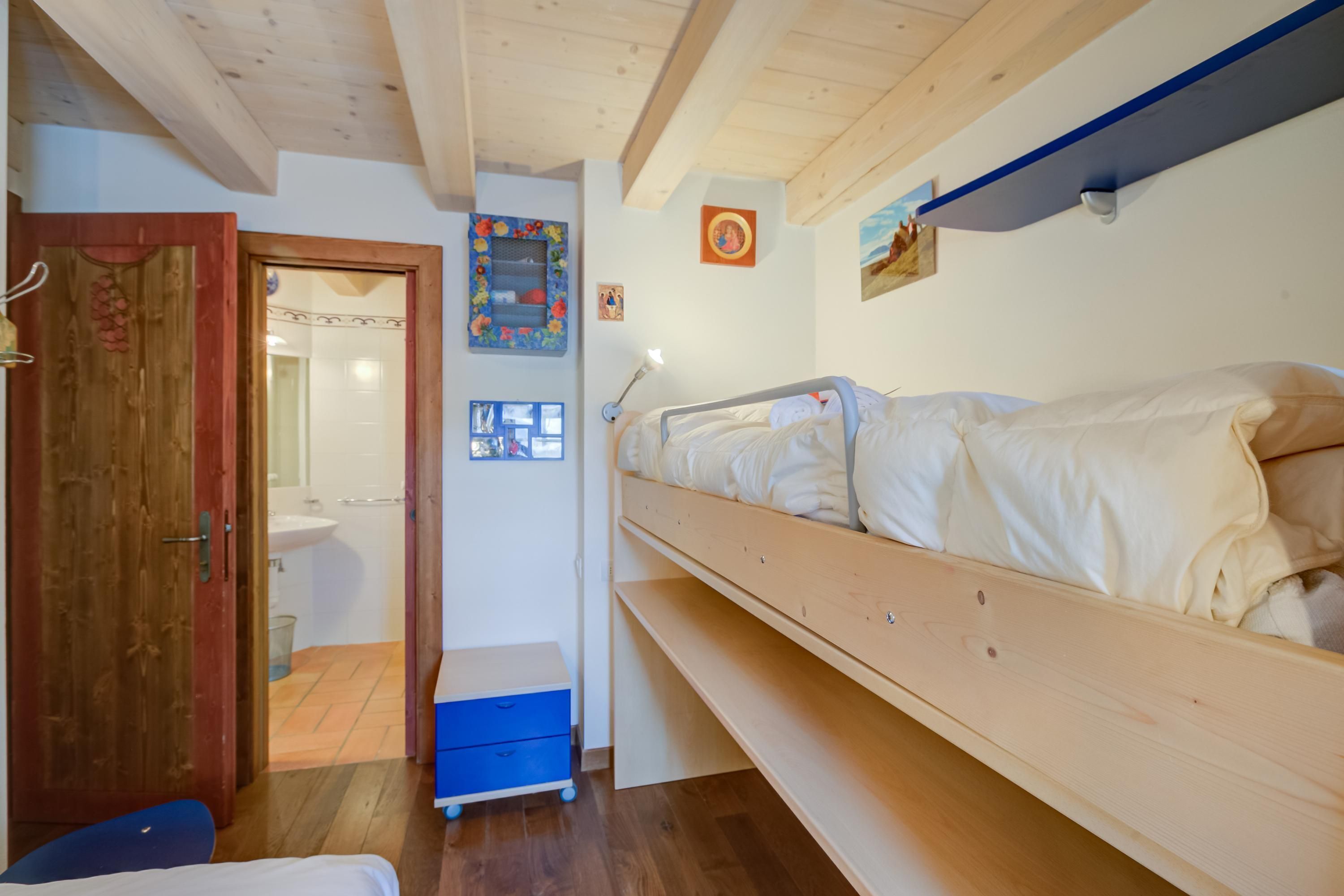 A bedroom with a wooden bunk bed, a small desk, a blue chair, and a wooden door.