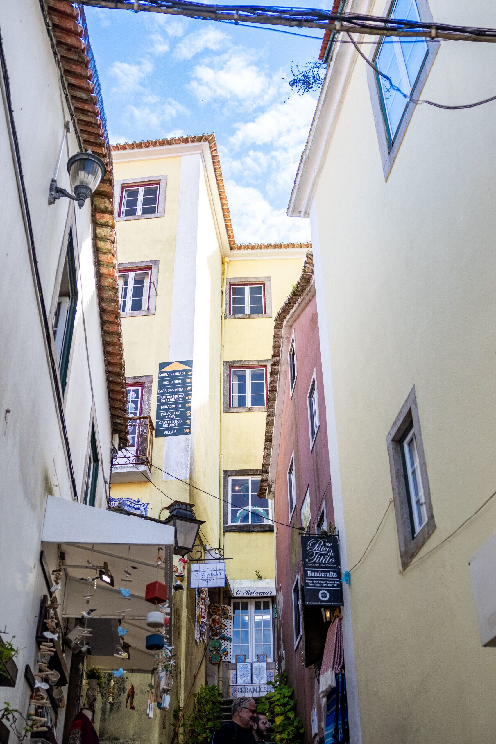 A narrow street with buildings on either side, featuring a variety of shops and signs.
