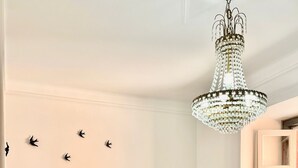 Una sala de estar acogedora con un sofá de color gris claro, cojines rojos, una mesa de centro de madera, una araña y cuadros en la pared.