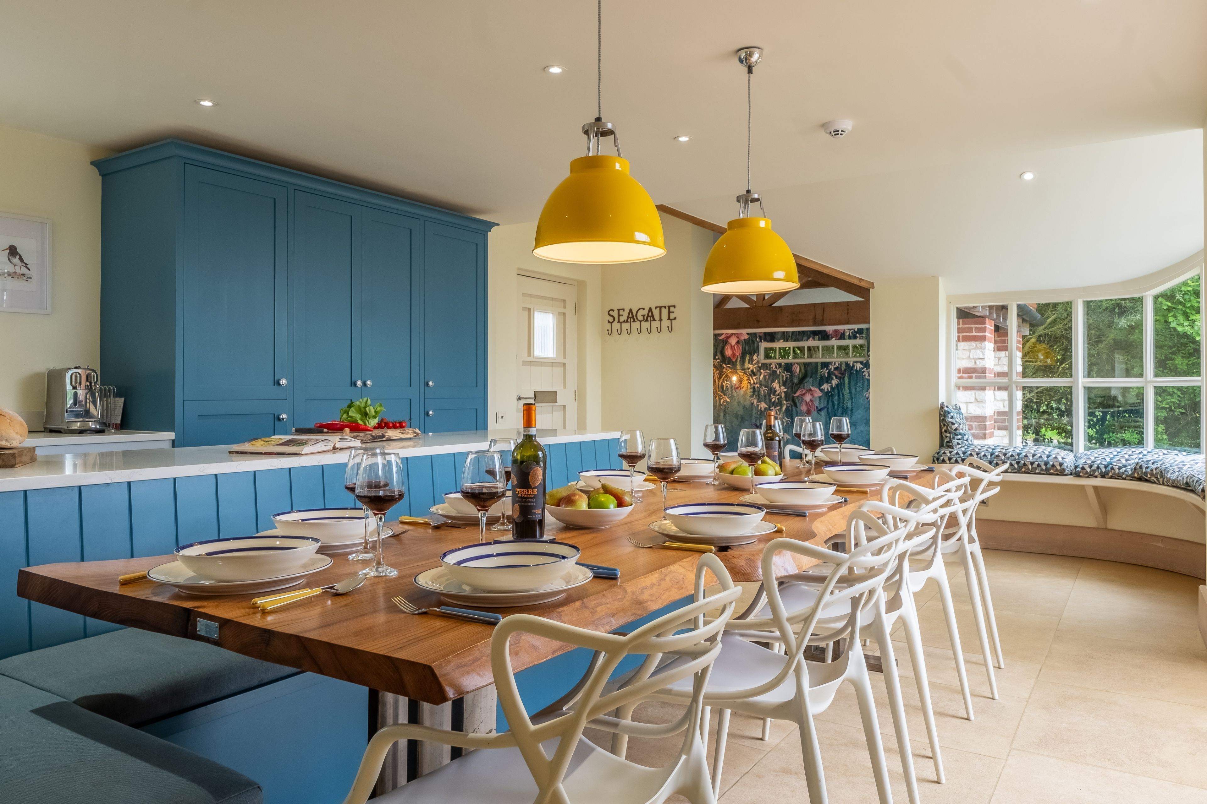A modern kitchen with blue cabinets, a wooden dining table set with plates, glasses, and a bottle of wine.