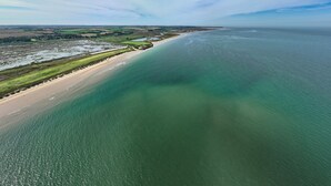 An aerial view of a coastal area with a sandy beach, green fields, and a large body of water. - Seagate House, Brancaster, Norfolk (Brancaster)