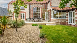 A two-story house with a stone facade, a tiled roof, and a patio with outdoor furniture. - Seagate House, Brancaster, Norfolk (Brancaster)