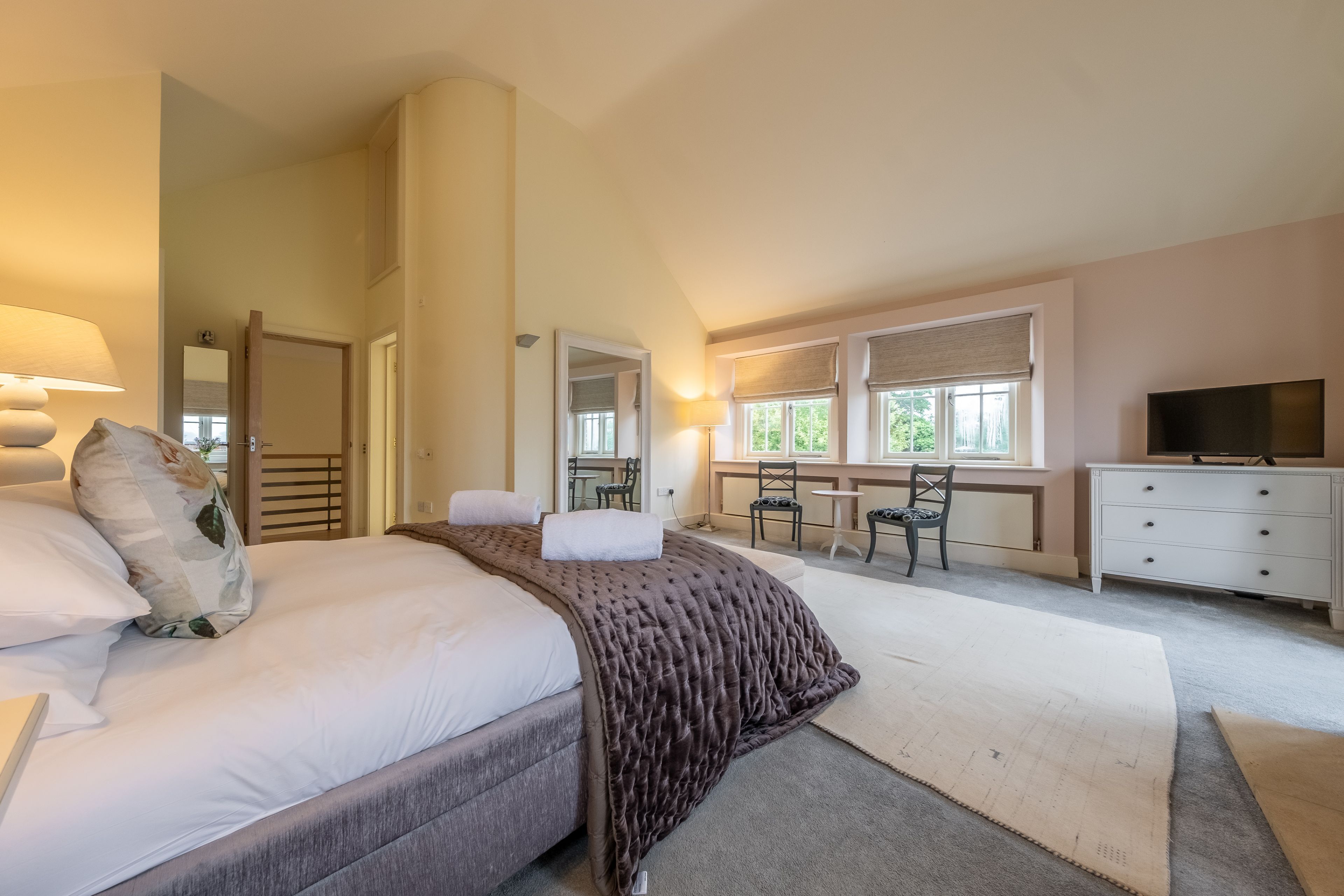 A bedroom with a bed, a desk, a chair, a TV, and a dresser.
