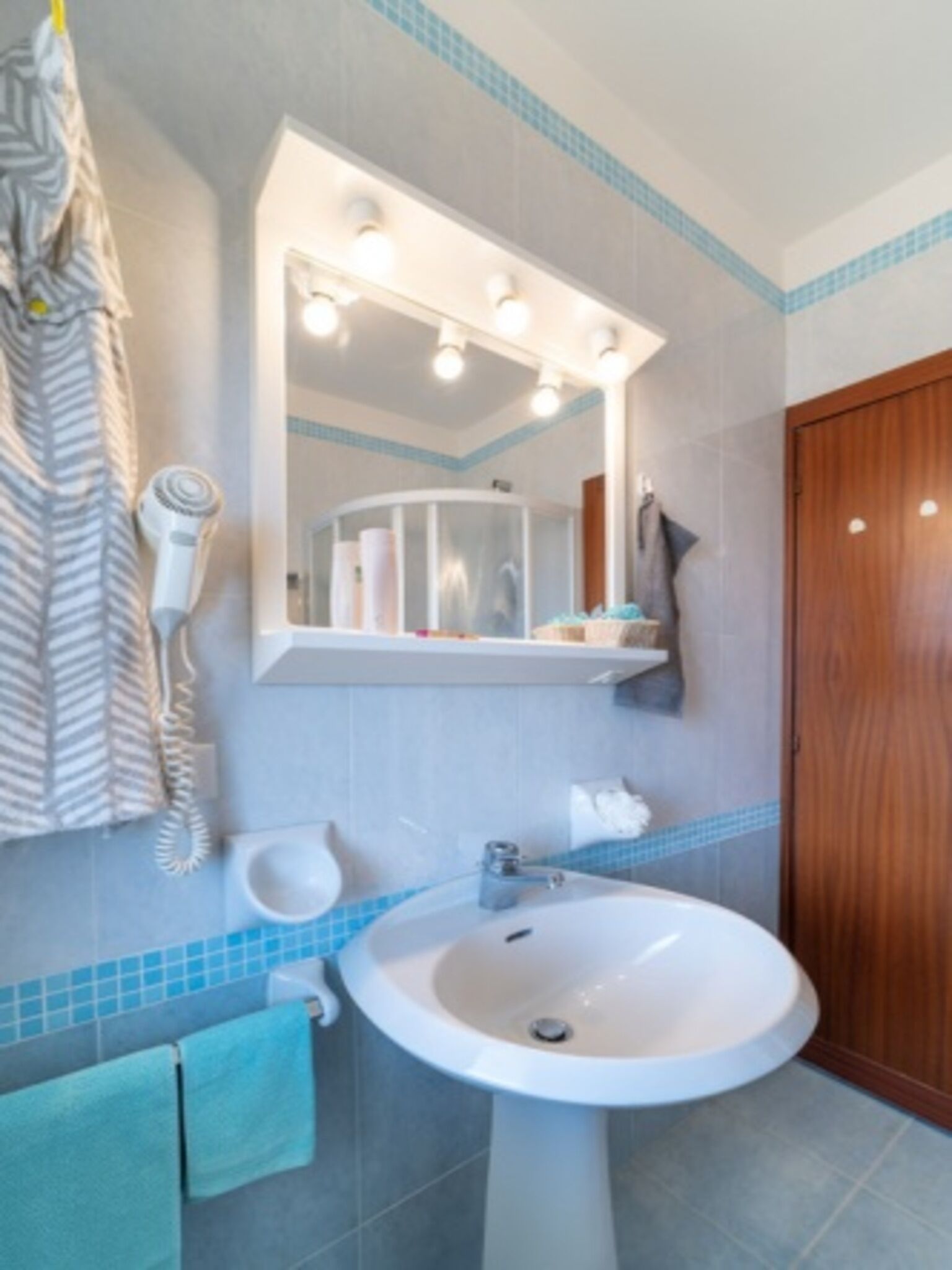Une salle de bain équipée d’un lavabo, d’un miroir, d’un porte-serviettes et d’un sèche-cheveux fixé au mur.