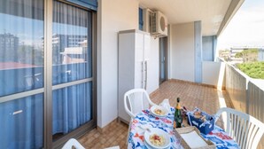 Ein Balkon mit Tisch für zwei Personen, einem Kühlschrank und einem Fenster mit Vorhängen.