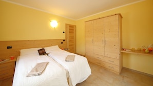 Un dormitorio con un armario de madera, una cama con ropa de cama blanca y una mesita de noche con una lámpara.