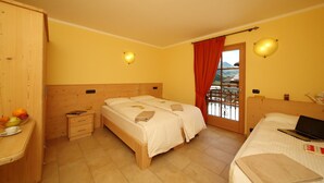 Habitación de hotel con dos camas, un armario de madera, una mesita de noche con frutero y una ventana con vistas a las montañas.