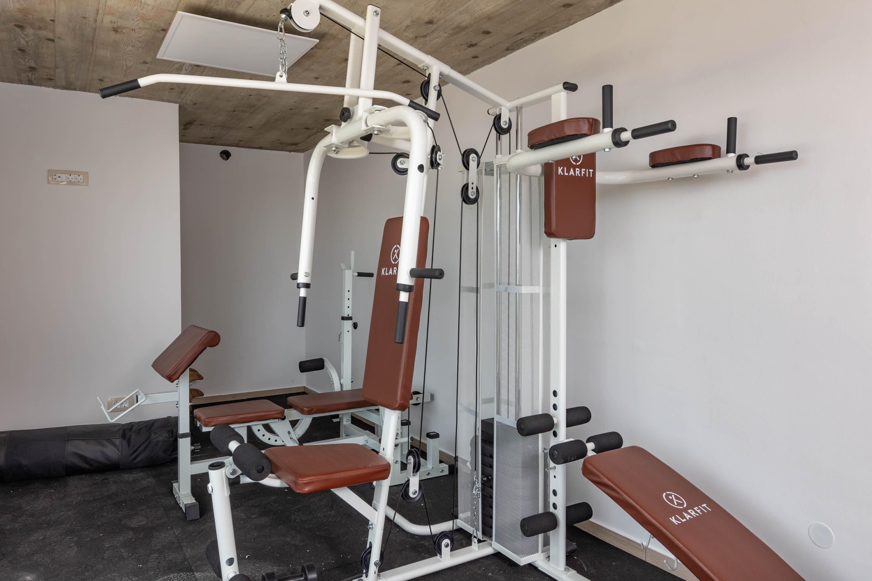 Un gimnasio con una prensa de banca, una máquina de poleas y una estructura para sentadillas.