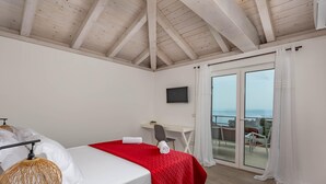 Een slaapkamer met een bed, een bureau, een stoel, een televisie en een balkon met gordijnen.