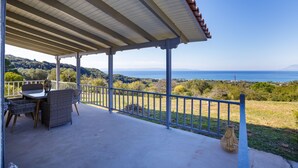 A covered outdoor area with a table and chairs, a railing, and a view of the sea and hills. - Villa Filokalia With Exceptional View (Andravida-Kyllini)