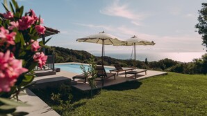 A poolside area with lounge chairs and umbrellas, overlooking a body of water and hills. - Villa Filokalia With Exceptional View (Andravida-Kyllini)