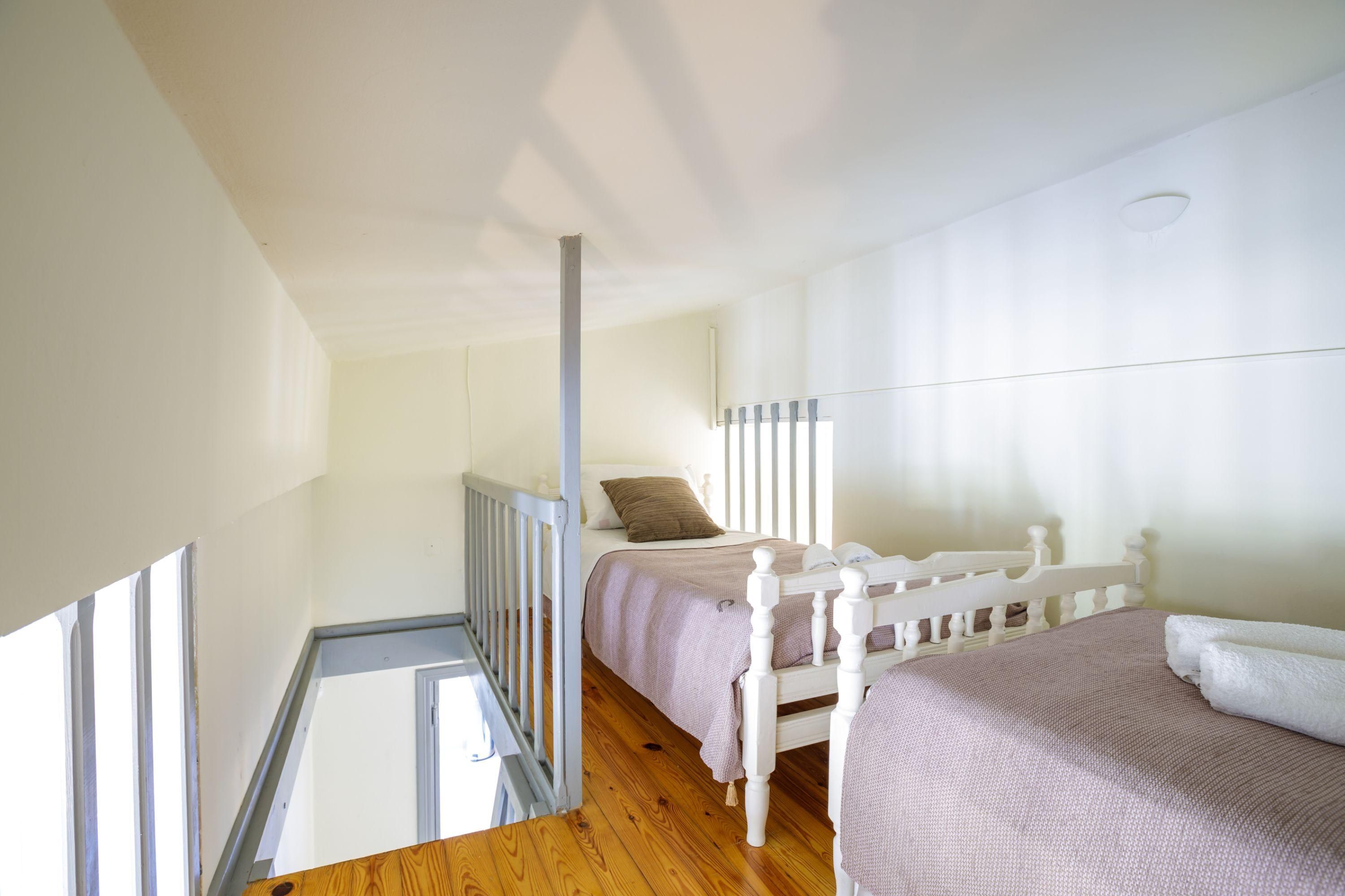 Une chambre avec un plancher en bois, des cadres de lit blancs et une tête de lit blanche.