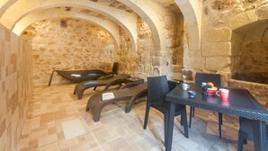 Una habitación con paredes de piedra, suelo a cuadros, una mesa con sillas y una mesita con un cuenco y una taza.