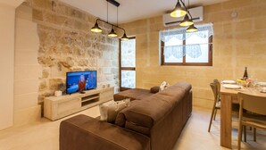 Una sala de estar con pared de piedra, un sofá marrón, un televisor y un comedor con mesa y sillas.
