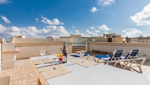 Una terraza al aire libre con una mesa preparada para dos personas, dos sillones de relax y una botella de vino.
