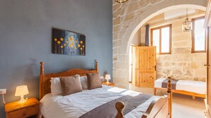 Ein Schlafzimmer mit einem großen Bett, einem Nachttisch mit Lampe, einem Holzschrank und einer Steinwand.