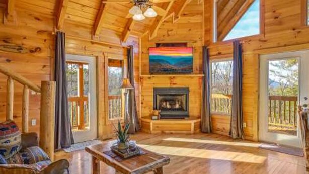 A log cabin interior with a fireplace, wooden floors, and large windows. - Spectacular Secluded Fire Pit Arcade Jacuzzi (Sevierville)