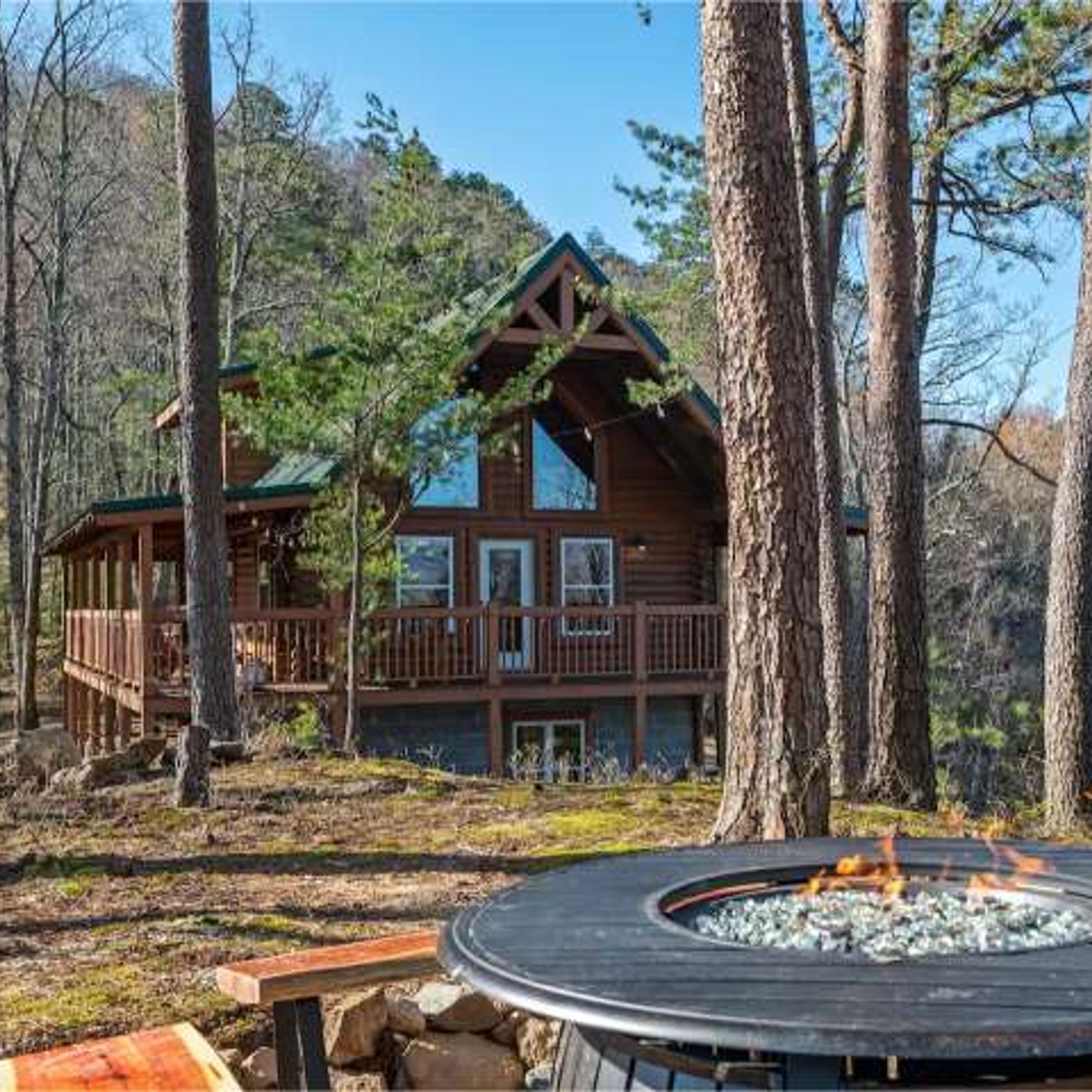 A cabin with a deck, a fire pit, and a forested backdrop.