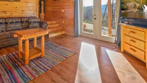 A wooden cabin interior with a sofa, a table, a television, and a sliding glass door leading to a balcony. - Spectacular Secluded Fire Pit Arcade Jacuzzi (Sevierville)
