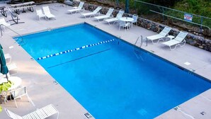 Una piscina rectangular con borde azul, rodeada de sillas reclinables blancas y un muro de piedra.