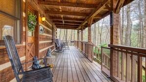 Une véranda en bois avec une balustrade, des sièges d’extérieur et une vue sur la forêt.