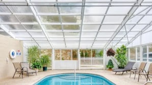 Piscina com teto de vidro, rodeada por espreguiçadeiras e plantas em vasos.