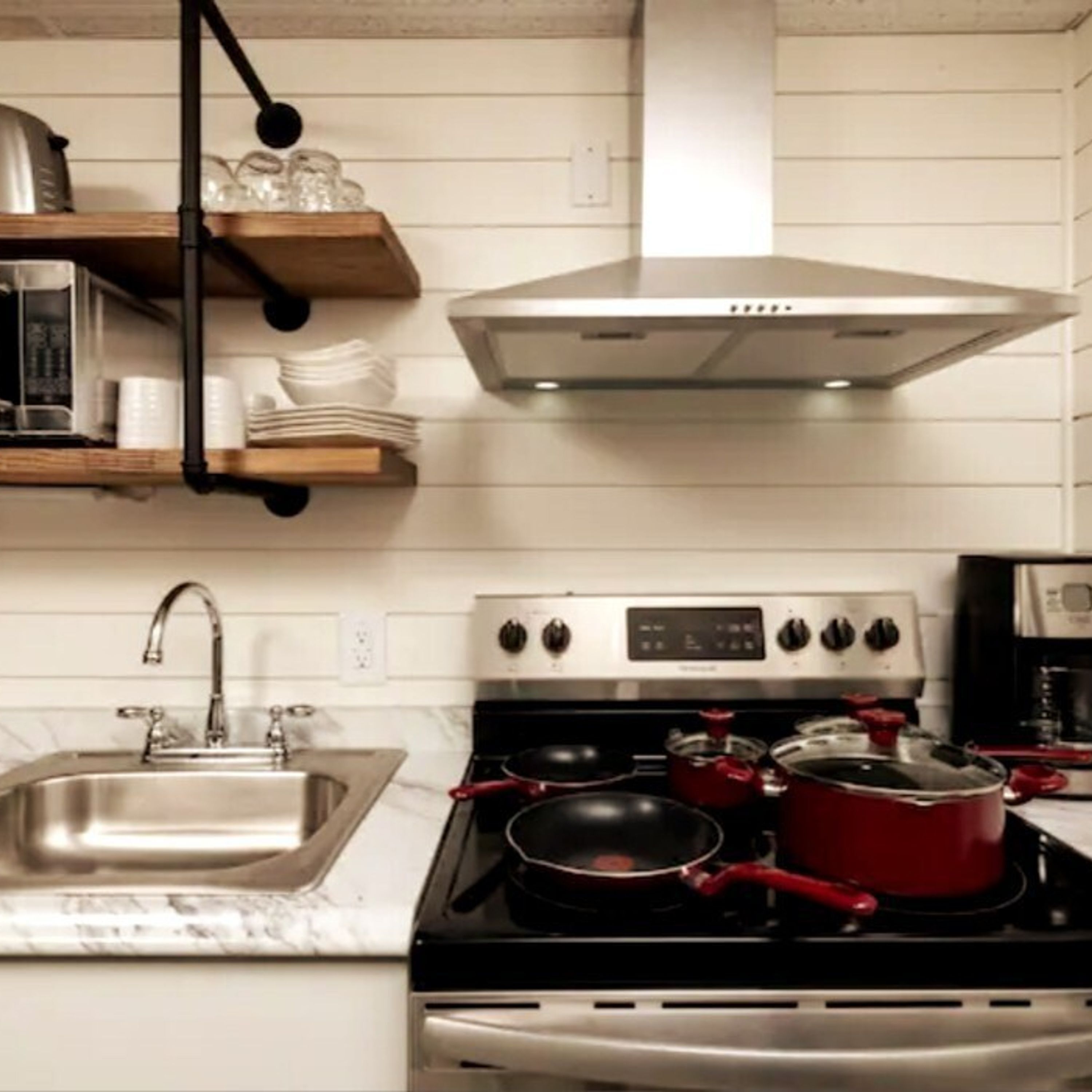 A kitchen with a stainless steel sink, a stove with pots, and a range hood above the stove.