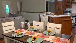 A dining area with a wooden table set for four, white chairs, and a floral table runner. - Pet Friendly Fire Pit Movie Theater Pool Sauna (Sevierville)