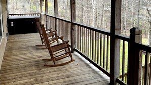 A wooden deck with a railing, a ceiling fan, and a view of a forested area. - Pet Friendly Fire Pit Movie Theater Pool Sauna (Sevierville)