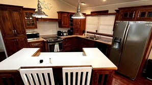 A kitchen with wooden cabinets, a stainless steel refrigerator, and a central island with two white chairs. - Pet Friendly Fire Pit Movie Theater Pool Sauna (Sevierville)