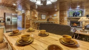 A wooden cabin interior with a dining table set for four, a fireplace, and a television mounted on the wall.