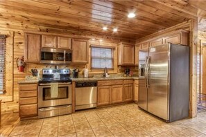 A kitchen with wooden cabinets, stainless steel appliances, and a tiled floor. - Dreams Come True With This Luxury Cabin (Gatlinburg)