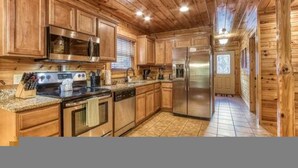 A wooden cabin-style kitchen with built-in appliances, a granite countertop, and a tiled floor.